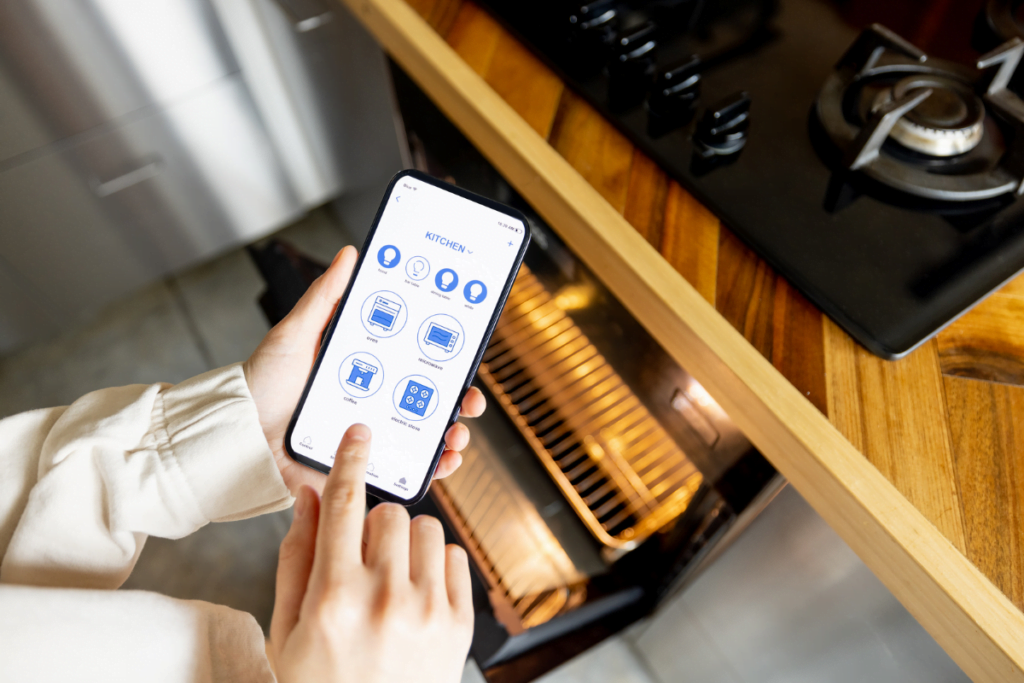 A woman utilizing a smart phone to manage an oven in a modern kitchen, showcasing the latest kitchen trend.