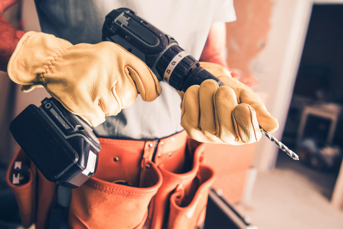 A person wearing yellow gloves using a cordless drill.