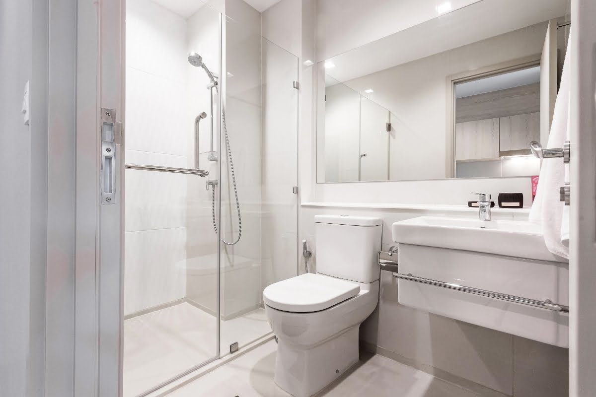 Safe Bathroom for Elderly: Design Tips for Aging-in-Place 1 Modern bathroom interior with glass shower enclosure, white toilet, sink, mirror, towel rail, and features ensuring a safe environment for the elderly.