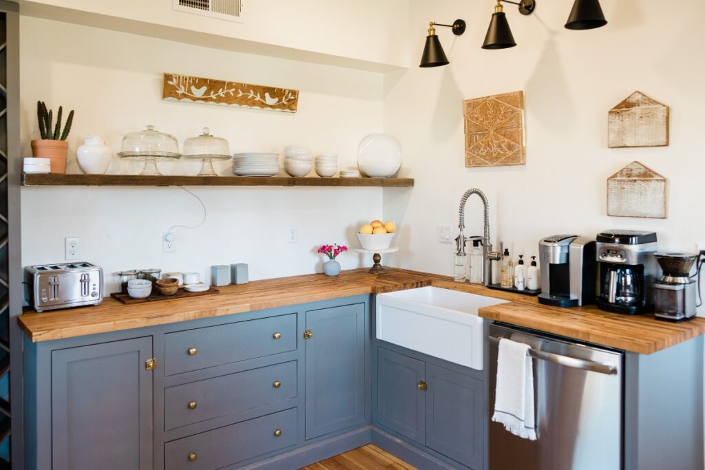 A modern kitchen with gray cabinets, wooden countertops, and open shelving displaying various dishes and kitchen maintenance tips.