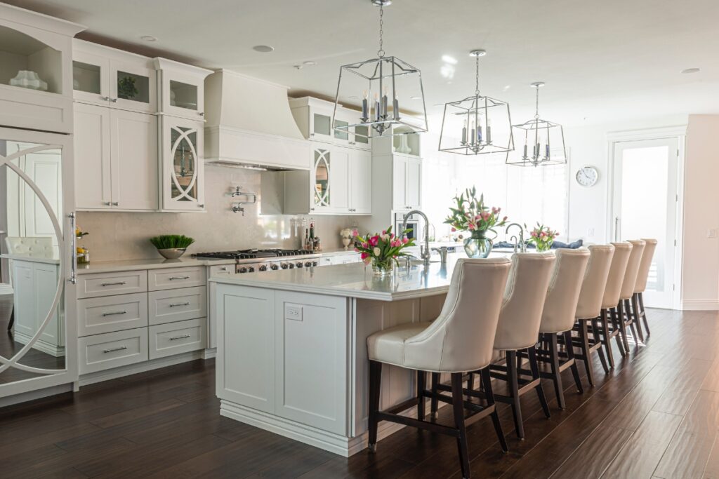 Modern kitchen maintenance tips, featuring white cabinetry, a central island with bar stools, pendant lights, and floral decorations.