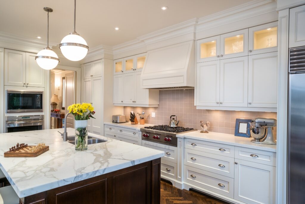 Modern kitchen maintenance tips with white cabinetry, marble countertops, stainless steel appliances, and pendant lighting.