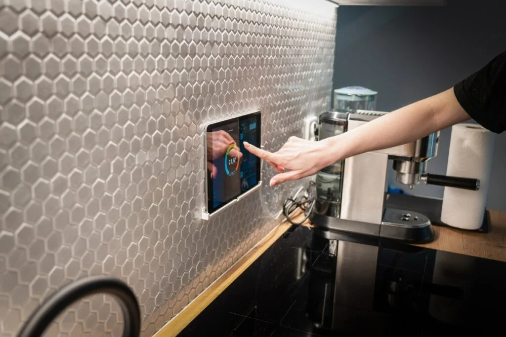 Smart Kitchen Technology: Revolutionizing Kitchens with Home Tech Integration 4 A person's hand adjusting a wall-mounted digital tablet displaying a timer in a smart kitchen with hexagonal tiles.