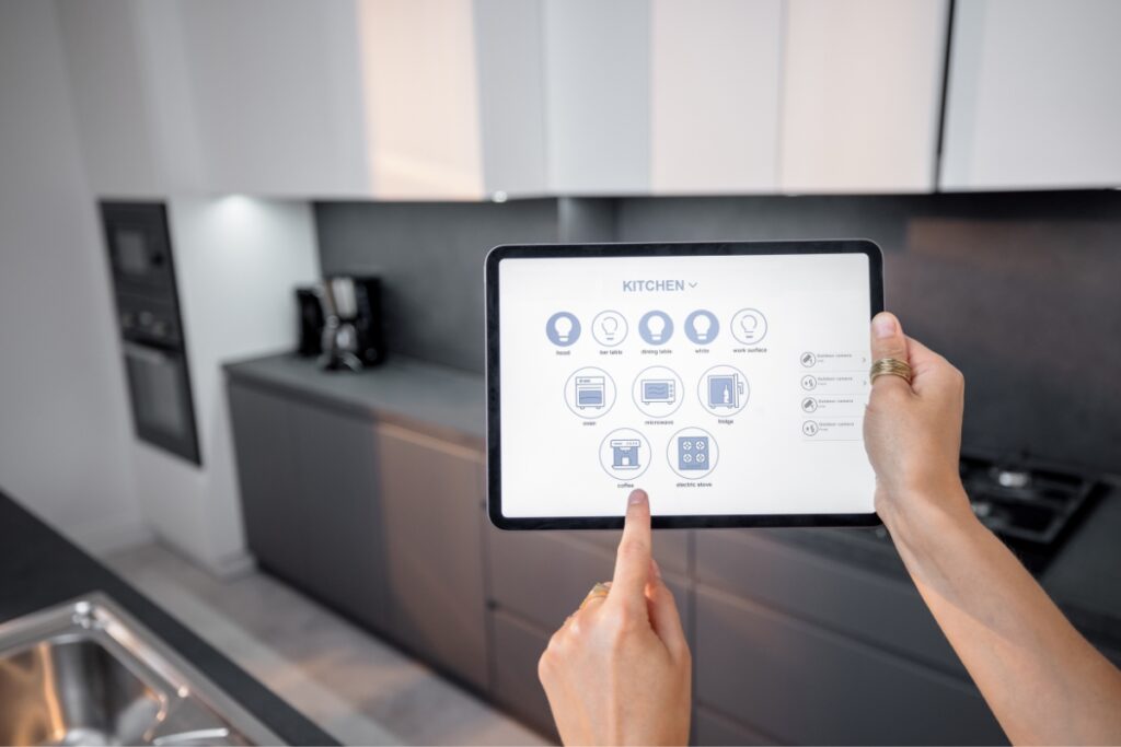 A person's hand holding a tablet displaying Smart Kitchen Technology for controlling kitchen appliances in a modern kitchen setting.