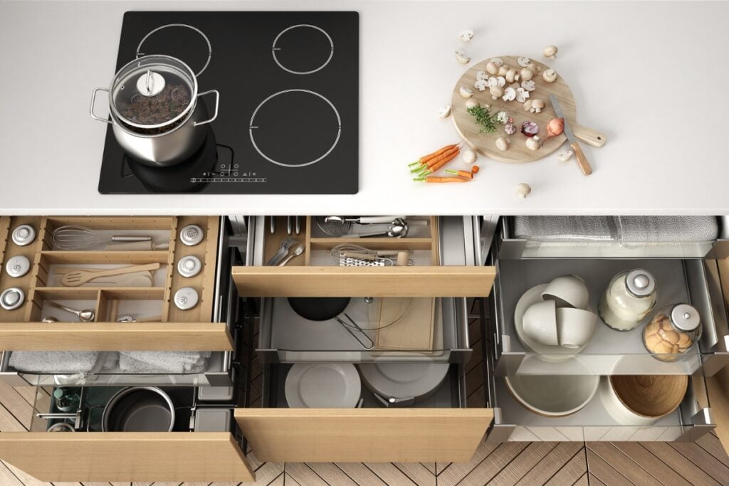 Top-down view of an organized kitchen counter and drawers featuring utensils, a cutting board with vegetables, and a cooking pot on a stovetop, reflecting the latest kitchen design trends.