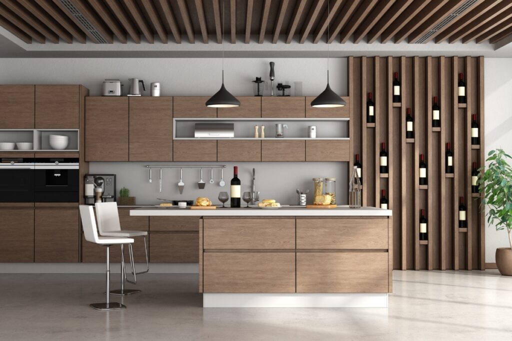 Modern kitchen with wooden cabinets, an island with two stools, hanging pendant lights, and a wine rack on the right wall. A potted plant is placed on the right, reflecting current kitchen design trends.