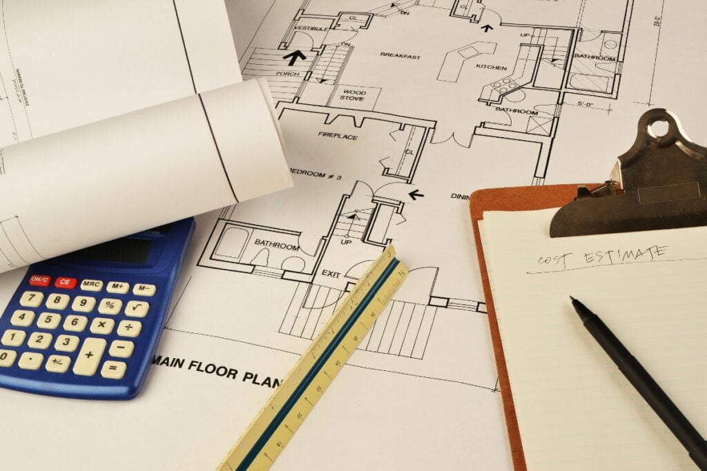 Architectural floor plan with a calculator, rolled blueprint, ruler, and clipboard holding a cost estimate sheet for an Atlanta real estate renovation.