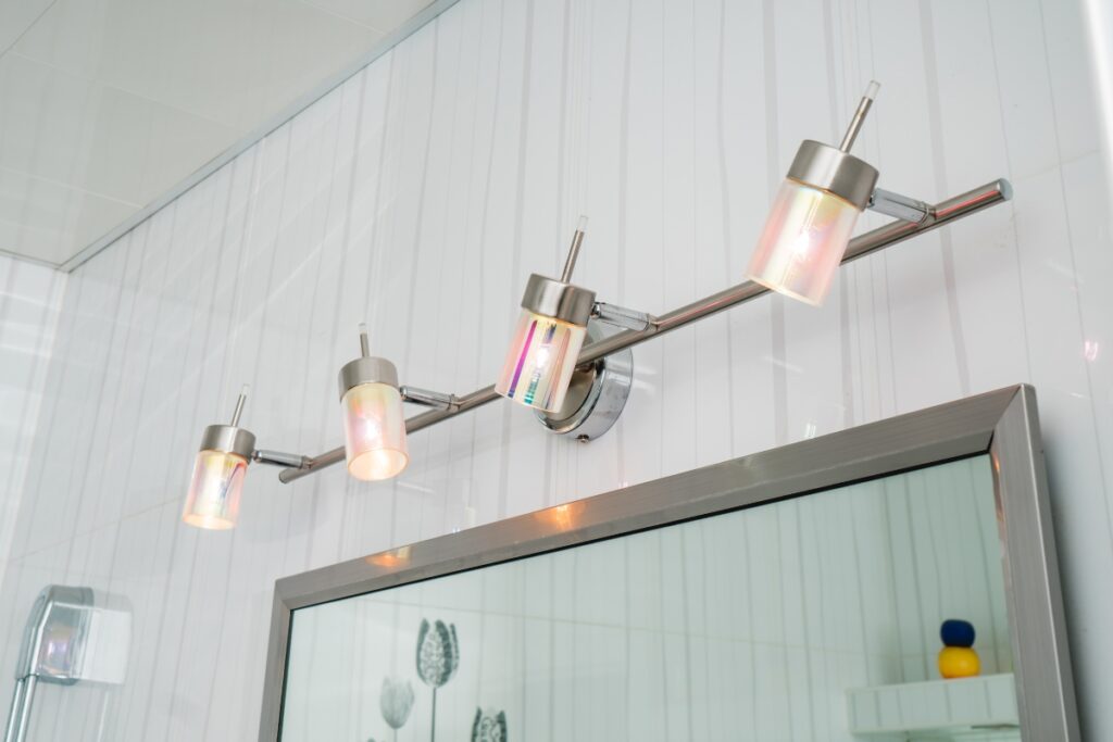 A modern bathroom light fixture with four cylindrical lights mounted above a rectangular mirror. The lights have a slightly tinted glass cover and are attached to a metallic bar, making it perfect for those seeking chic DIY bathroom projects.