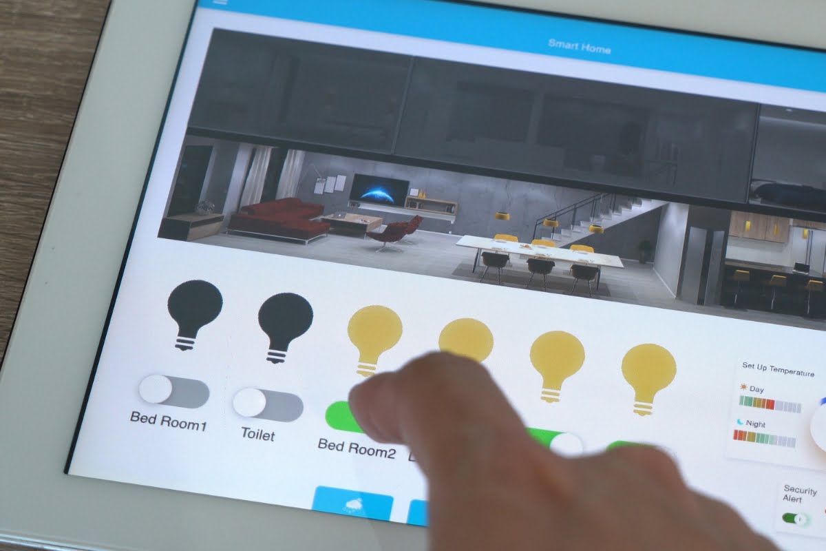 A person uses a tablet to control the lighting in a smart home. The screen, part of advanced home automation systems, shows options to manage lights in various rooms including Bedroom 1 and Bedroom 2.