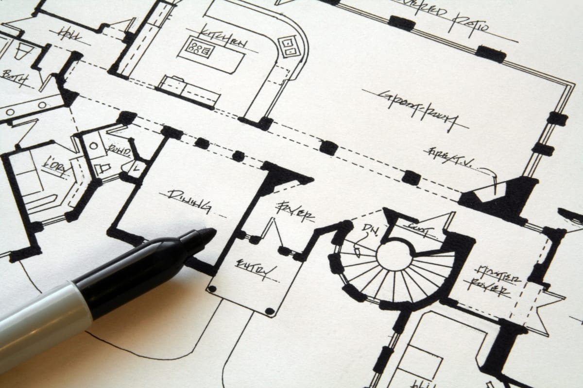 A black pen rests on a detailed architectural floor plan featuring cultural design elements and labeled rooms, including a kitchen, dining room, foyer, and stairs.