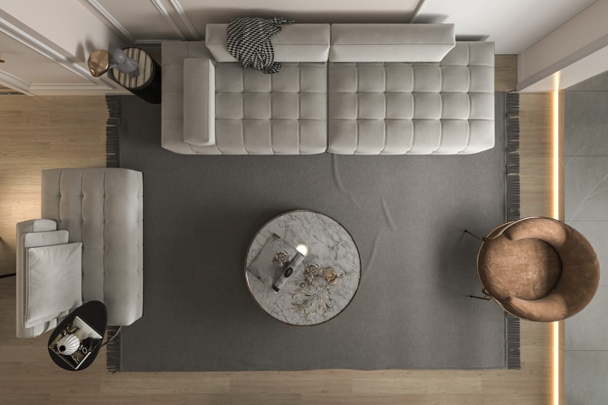 Top-down view of a modern living room featuring a grey tufted couch, a matching armchair, a round marble coffee table, a brown leather chair, and a grey rug on a wooden floor, showcasing subtle elements of cultural design.