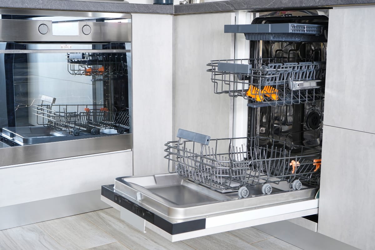 Open stainless steel dishwasher with racks extended, showcasing sleek kitchen appliances in a modern setting.