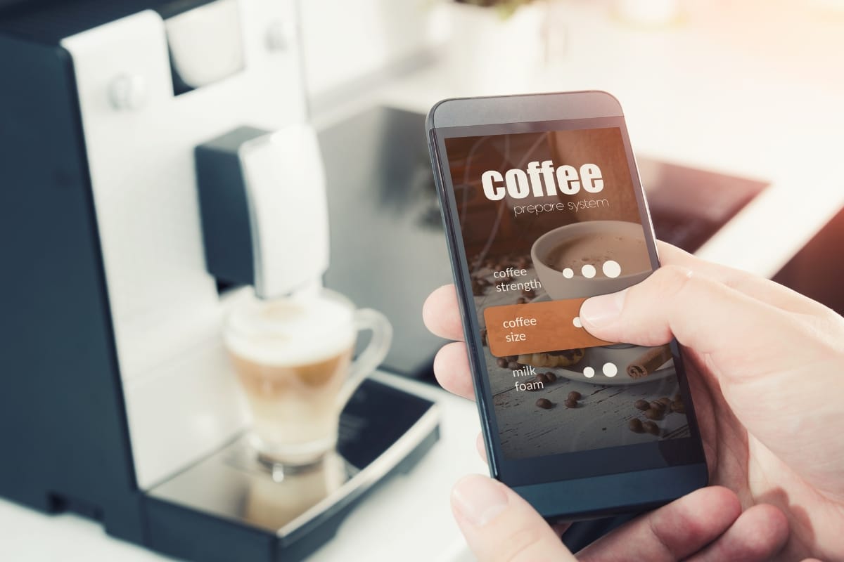 In the heart of a modern kitchen, a person uses a smartphone app to seamlessly adjust settings on the coffee machine, showcasing the harmony of technology and kitchen appliances. As they finalize their choices, the aroma of fresh coffee fills the air, hinting at perfection in every cup.