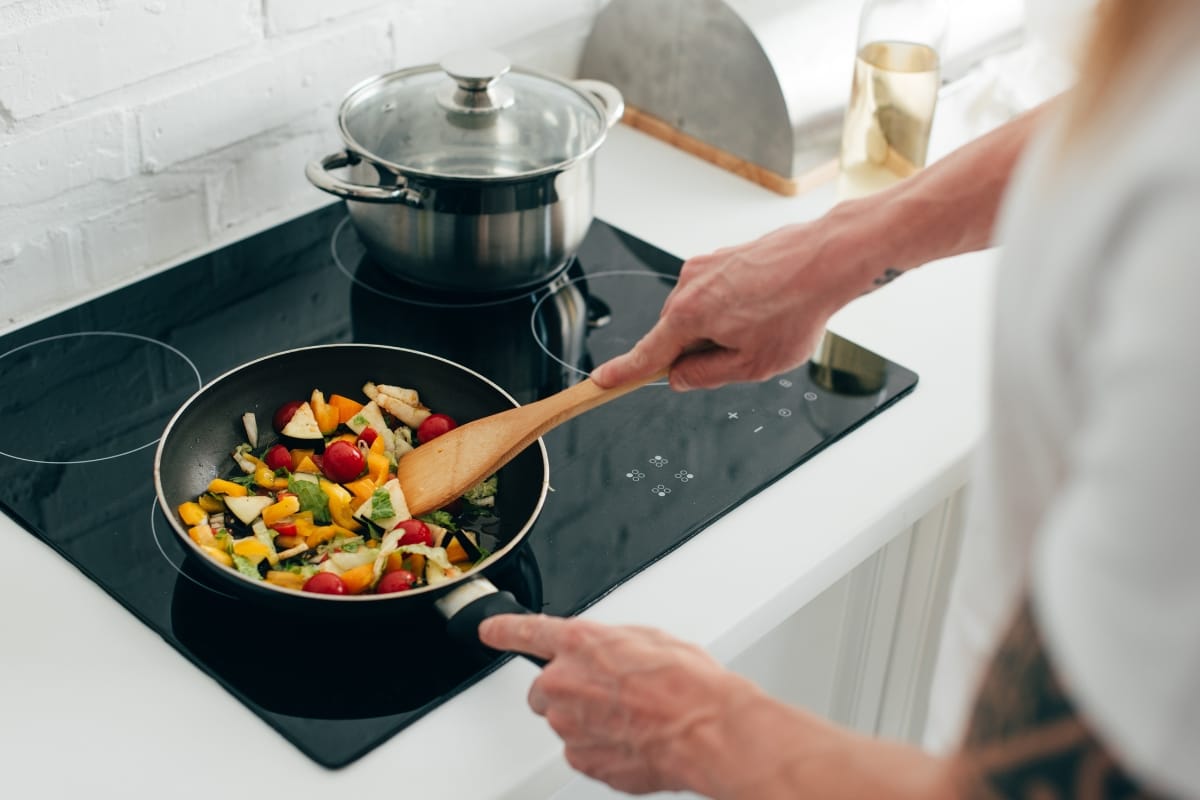 A person is cooking a colorful vegetable stir-fry in a pan on a modern stovetop, showcasing the seamless efficiency of contemporary kitchen appliances.