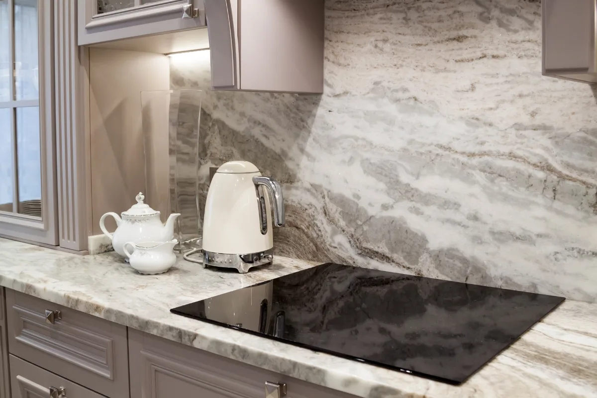 Top Kitchen Countertop Options for Your Sandy Springs Remodel 19 A marble kitchen countertop for Sandy Springs homeowners featuring a white teapot, matching sugar bowl, cream-colored electric kettle, and a flat electric stove.