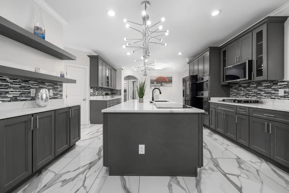 Top Kitchen Countertop Options for Your Sandy Springs Remodel 31 Modern kitchen with dark cabinets, white marble flooring, and a large central island showcasing key kitchen countertops. Contemporary lighting fixtures illuminate walls featuring geometric tiled backsplash and open shelves adorned with decor—a perfect setting for Sandy Springs homeowners.