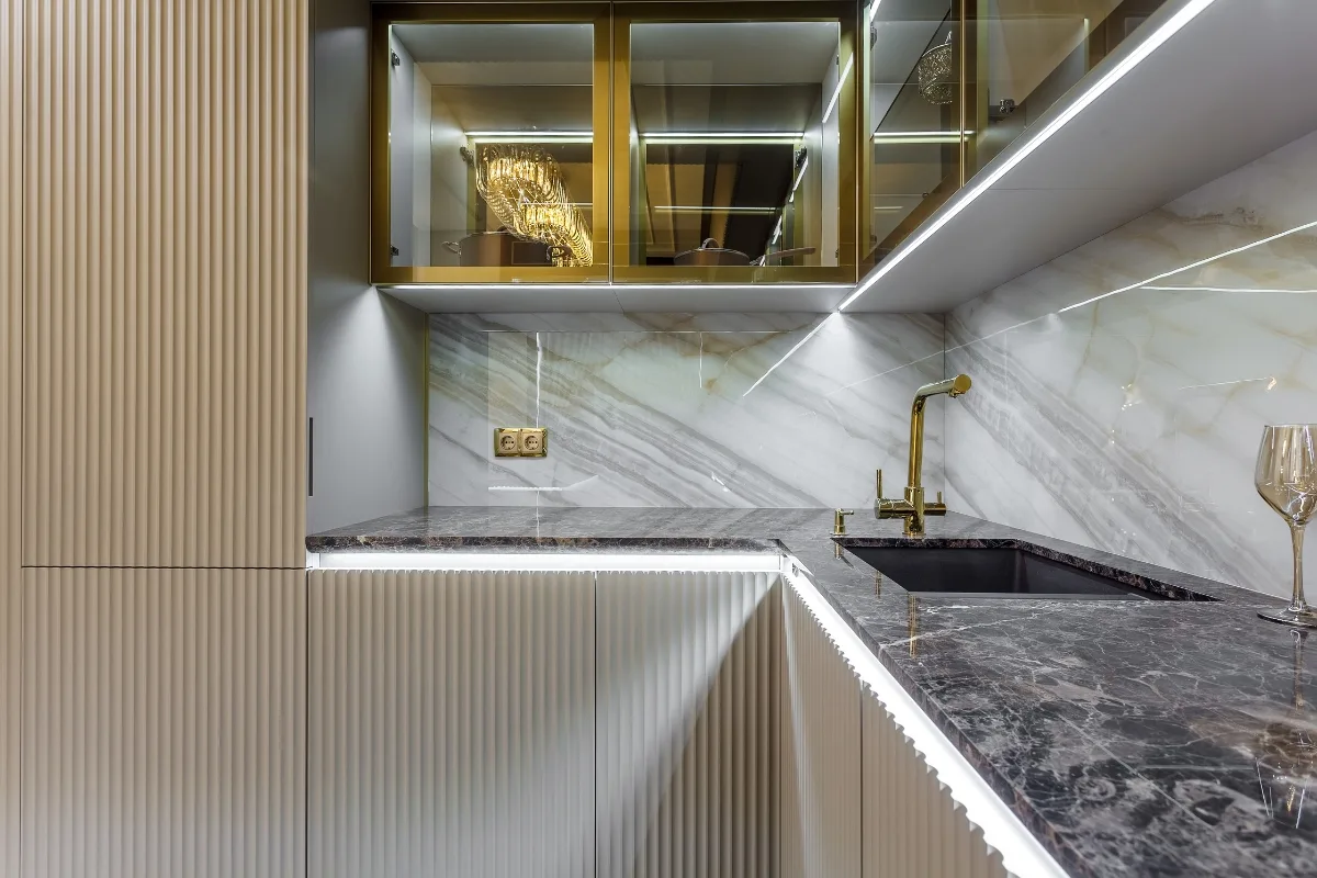 Top Kitchen Countertop Options for Your Sandy Springs Remodel 23 Modern kitchen with gold accents, marble backsplash, black sink, and glass cabinets. A wine glass sits on the key kitchen countertop under bright lighting—a chic choice for Sandy Springs homeowners seeking elegance.
