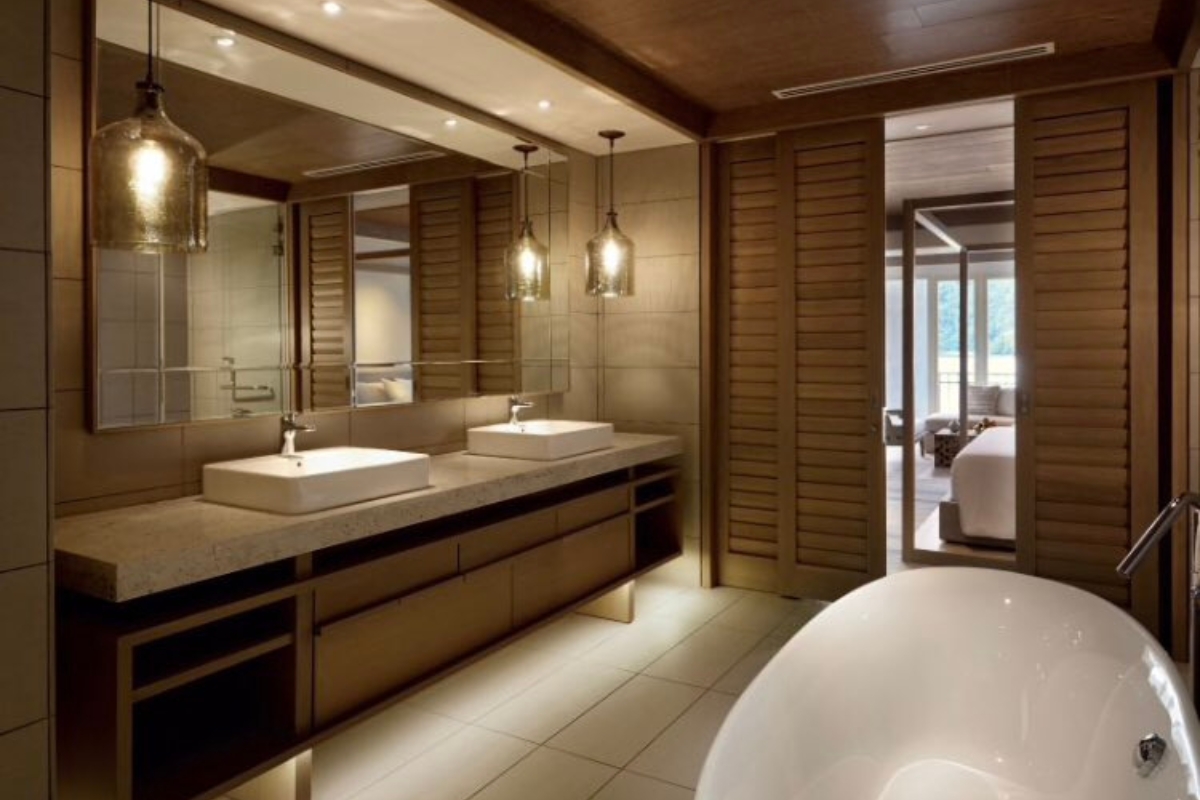 Elegant Bathroom Vanities in Roswell: Choosing the Right Style for Your Space 2 Modern bathroom with elegant bathroom vanities, double sinks, large mirrors, pendant lights, wooden accents, and a freestanding bathtub. Sliding shutter doors open to a bedroom filled with natural light.