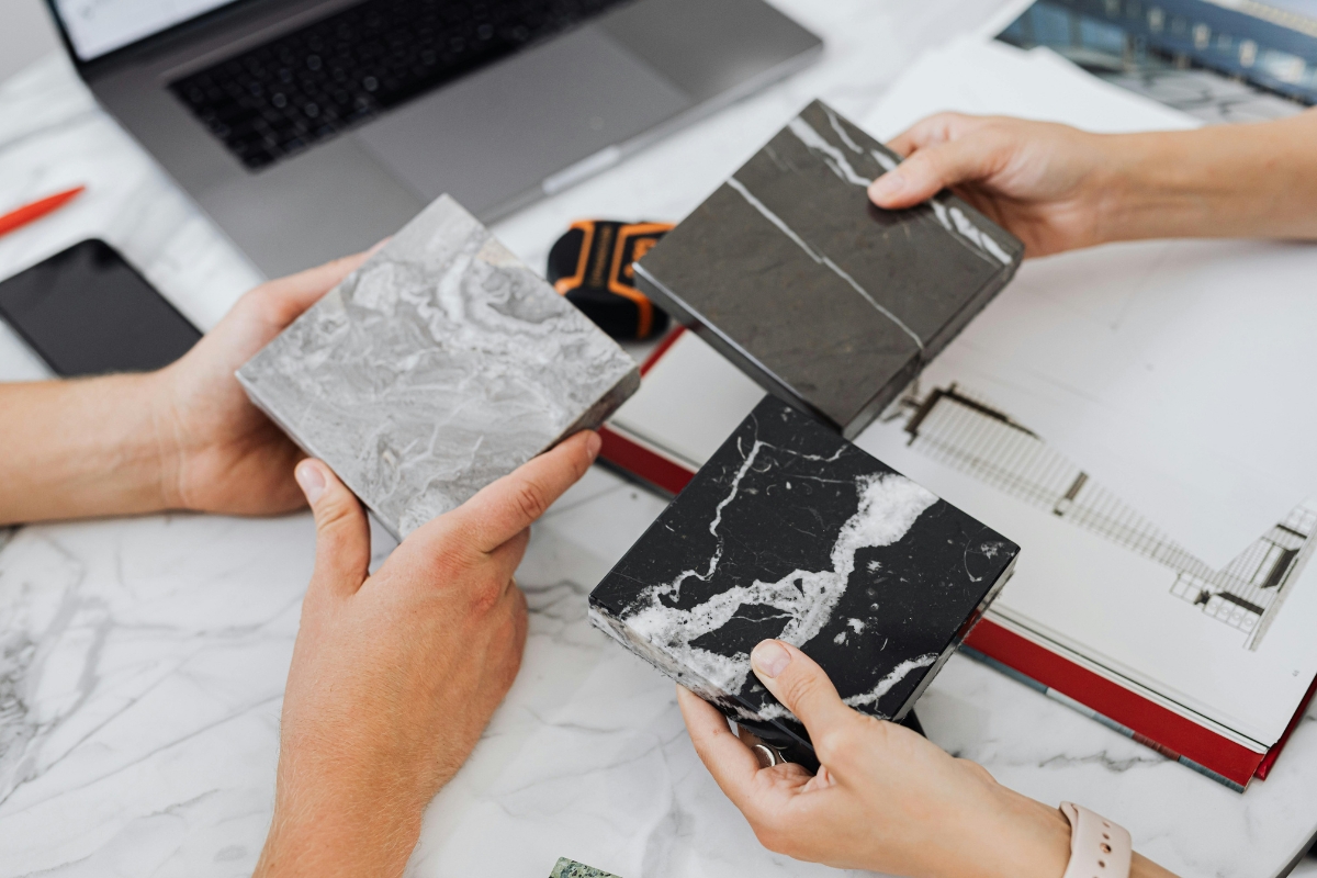 Bathroom Tile Flooring in Vinings: Expert Tips, Trends, and Benefits 4 Three people hold different bathroom tile flooring samples above a table with architectural plans, a laptop, and a smartphone.