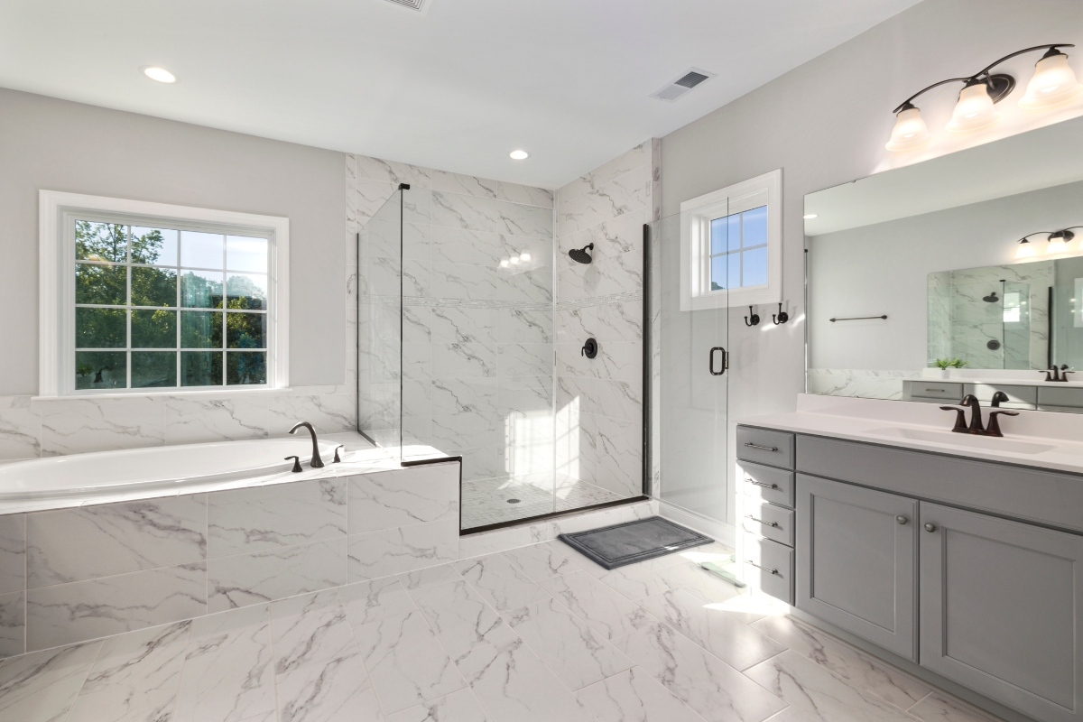 Bathroom Tile Flooring in Vinings: Expert Tips, Trends, and Benefits 8 Modern bathroom with a glass-enclosed shower, elegant bathroom tile flooring and marble walls, a built-in bathtub, large window, gray vanity with sink, and wall-mounted lights above the mirror.