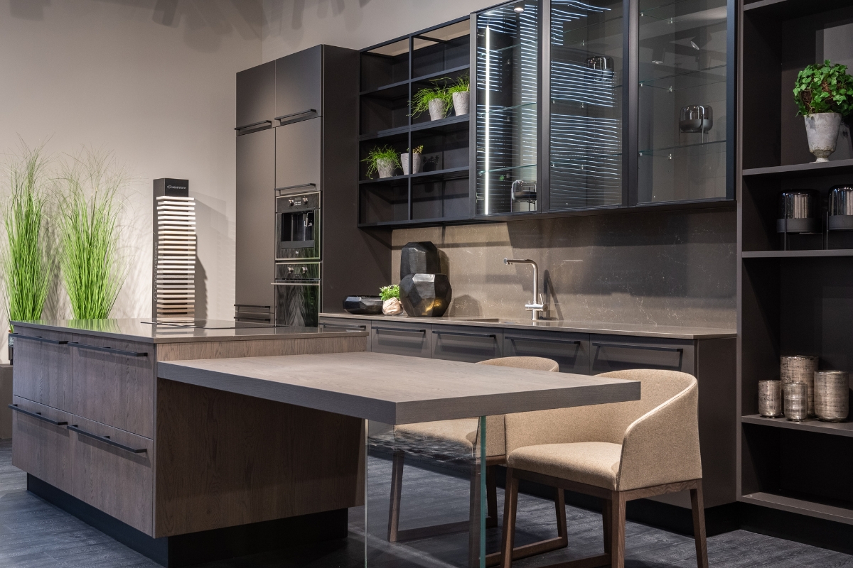 Custom Kitchen Storage Solutions in Kennesaw: Maximize Your Space 5 Modern kitchen with dark cabinets, open shelves, custom kitchen storage, built-in appliances, an island with an attached dining table, two chairs, and decorative plants.