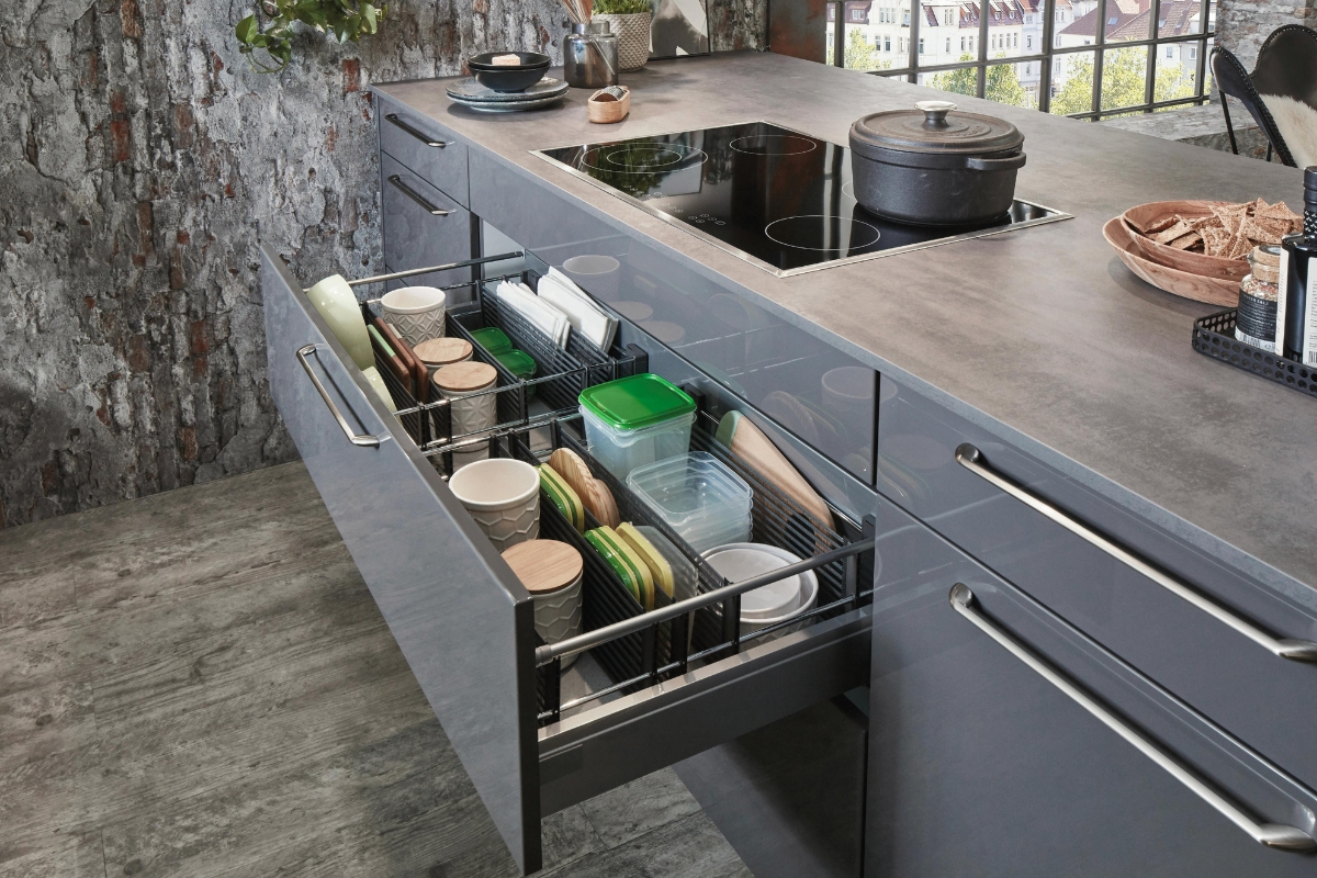 Custom Kitchen Storage Solutions in Kennesaw: Maximize Your Space 6 Open kitchen drawer with custom kitchen storage showcasing organized dishes, bowls, containers, and lids neatly arranged beneath a gray countertop and induction cooktop.