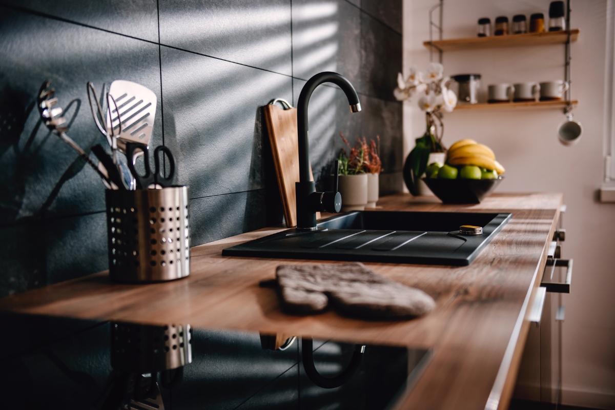 Luxury Kitchen Remodeling in Buckhead: Must-Have Features for 2025 9 Modern kitchen countertop with a black sink, faucet, utensils holder, cutting board, potted plants, bowl of fruit, and shelves with jars against a tiled backsplash—perfect for those seeking luxury kitchen remodeling inspiration.