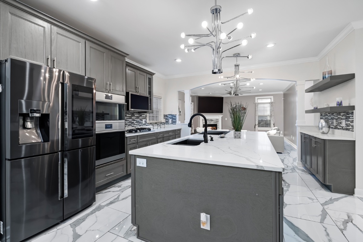 Luxury Kitchen Remodeling in Buckhead: Must-Have Features for 2025 2 Modern kitchen with gray cabinets, stainless steel appliances, marble countertops, a large island with sink, and contemporary lighting fixtures—an ideal example of luxury kitchen remodeling.