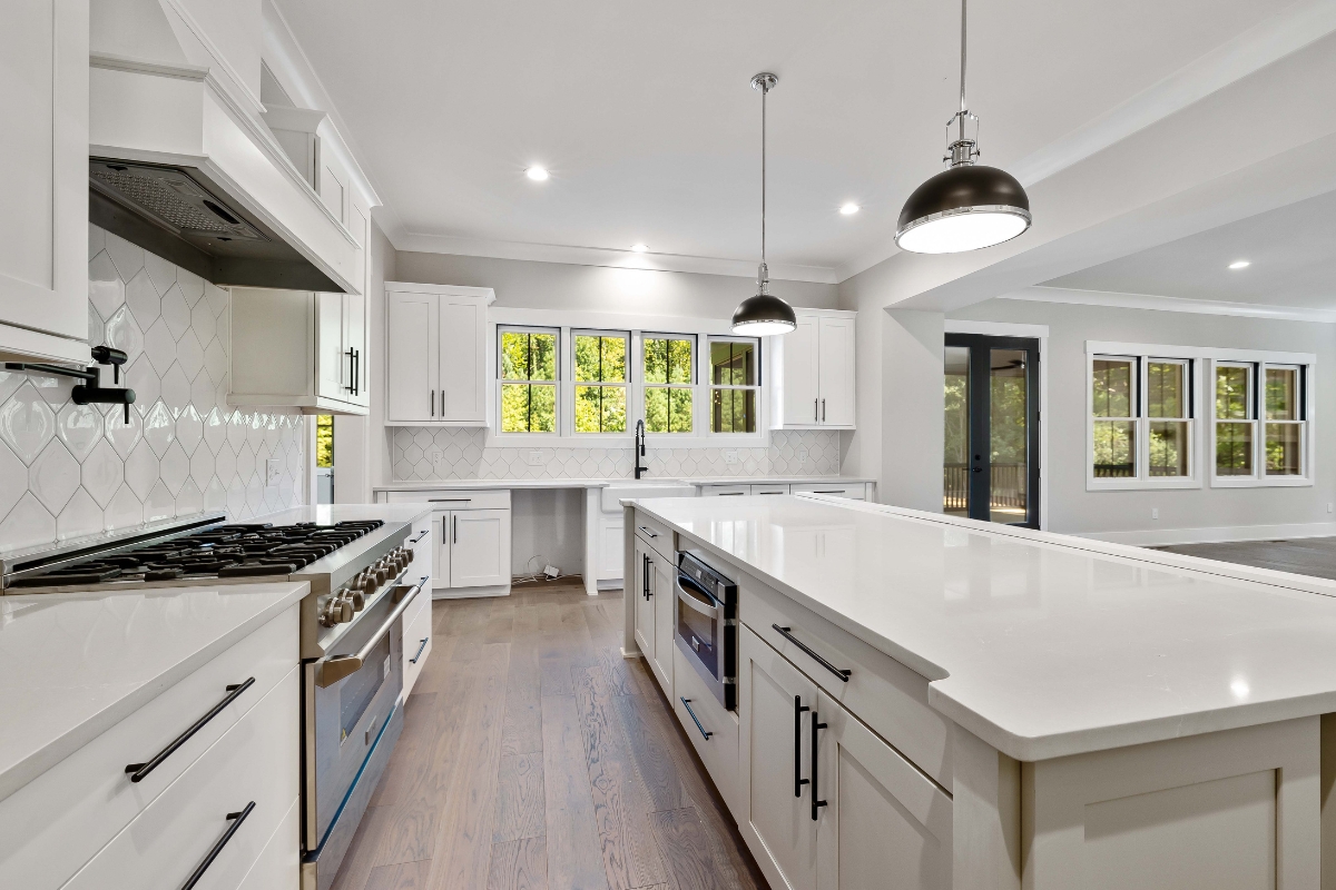 Eco-Friendly Kitchen Remodeling in Smyrna: Sustainable Upgrades That Last 18 Modern kitchen with white cabinets, stainless steel appliances, and a large island with built-in sink features pendant lights and windows overlooking greenery—an ideal space for eco-friendly kitchen remodeling.