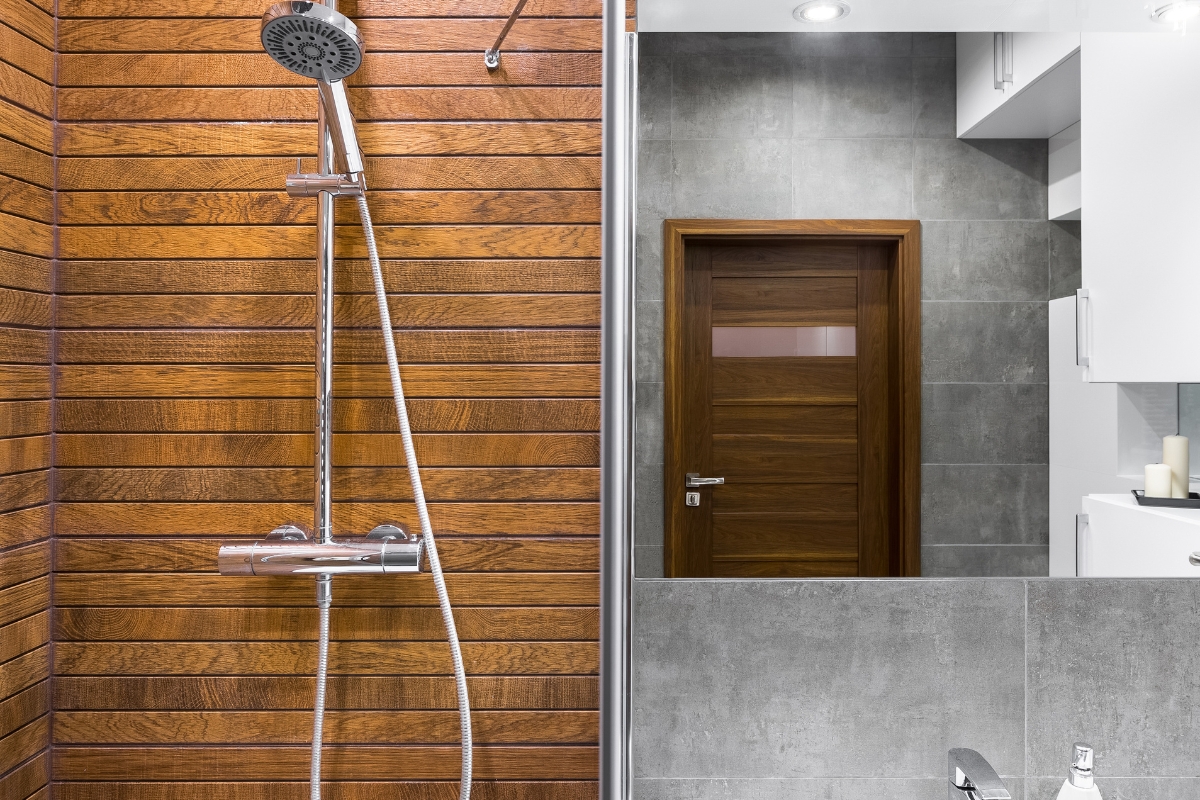 Shower Replacement in Sandy Plains: What to Expect and How to Prepare 6 Modern bathroom with a wood-paneled shower replacement on the left, gray tiled walls, a wooden door, and a partial view of a sink and mirror on the right.