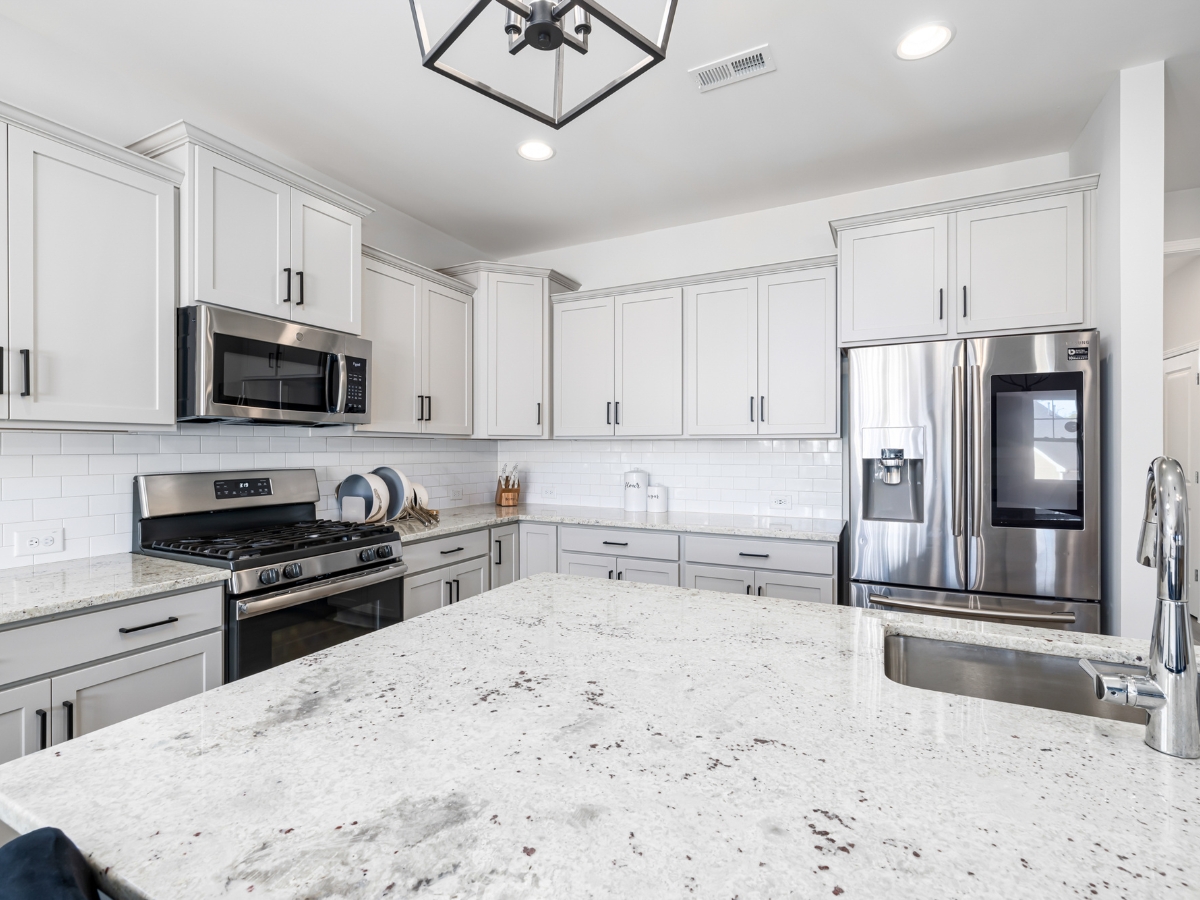 Quartz vs. Granite Countertops in Alpharetta: Which Should You Choose? 14 Modern kitchen with white cabinets, stainless steel appliances, gas stove, and a spacious island with a built-in sink under bright lighting—perfect for comparing Quartz vs. Granite Countertops in both style and functionality.