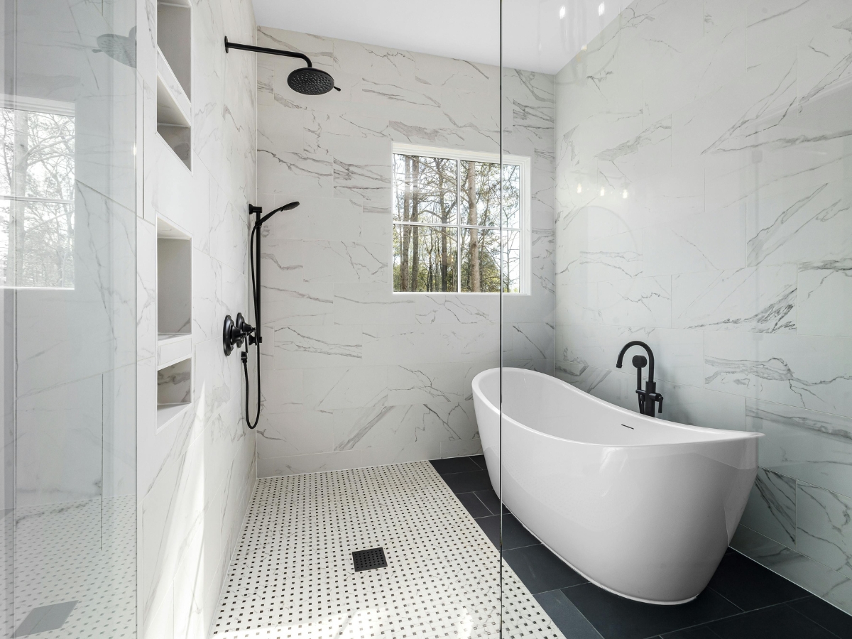 Bathroom Remodeling Trends in Atlanta-Midtown: Top Design Ideas for 2025 4 Modern bathroom with a freestanding white tub, black faucet, walk-in shower with rainfall showerhead, and white marble walls. Showcasing top bathroom remodeling trends, natural light enters through a window.