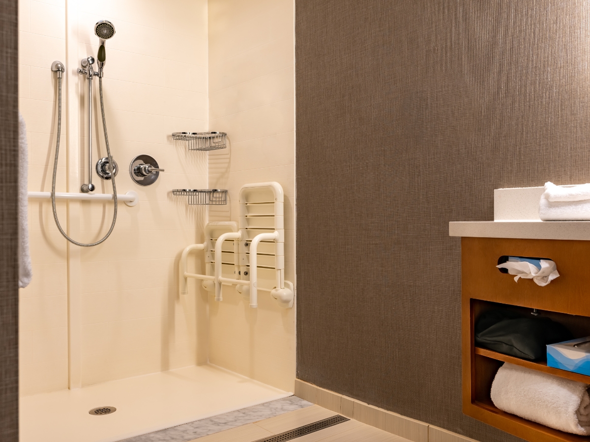 Bathroom Remodeling Trends in Atlanta-Midtown: Top Design Ideas for 2025 5 Accessible shower with grab bars, handheld showerhead, shower seat, and storage shelves reflects modern bathroom remodeling trends; adjacent vanity showcases towels and toiletries for added convenience.
