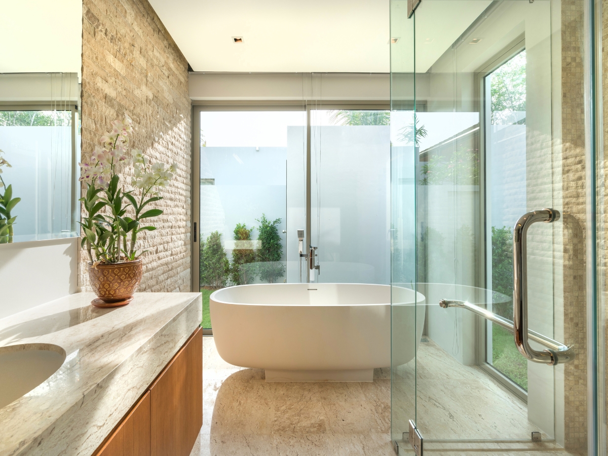 Bathroom Remodeling Trends in Atlanta-Midtown: Top Design Ideas for 2025 2 Modern bathroom with a freestanding bathtub, glass shower enclosure, marble countertop, potted plant, and large frosted windows facing a garden—showcasing the latest bathroom remodeling trends.