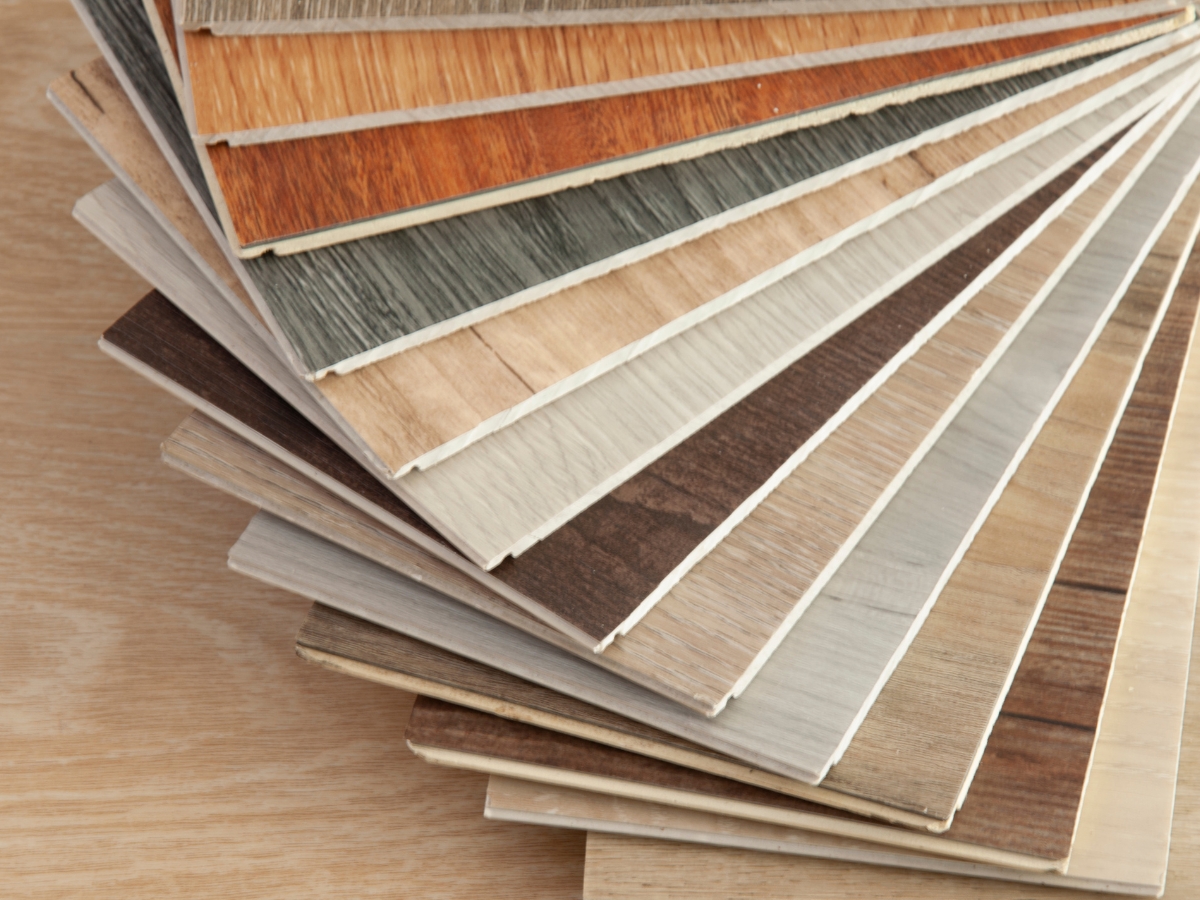 Custom Cabinetry vs. Stock Cabinets in Sandy Springs: Which Is Right for You? 4 A fanned-out selection of laminate flooring samples in various wood colors and finishes is displayed on a wooden surface, perfect for coordinating with custom cabinetry vs. stock cabinets in your home.