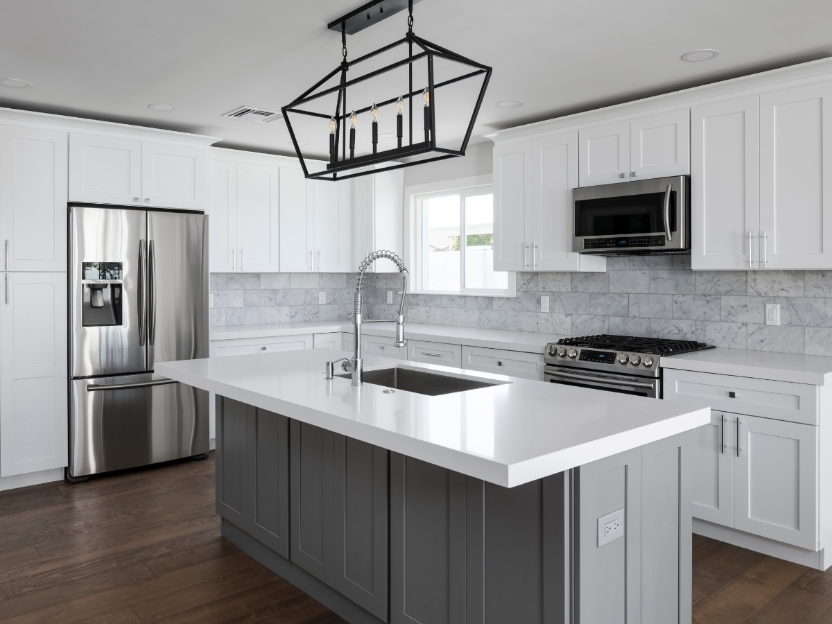 Custom Cabinetry vs. Stock Cabinets in Sandy Springs: Which Is Right for You? 5 Modern kitchen with white cabinets featuring custom cabinetry vs. stock cabinets, stainless steel appliances, a gray island with a sink, marble backsplash, and a black rectangular pendant light.