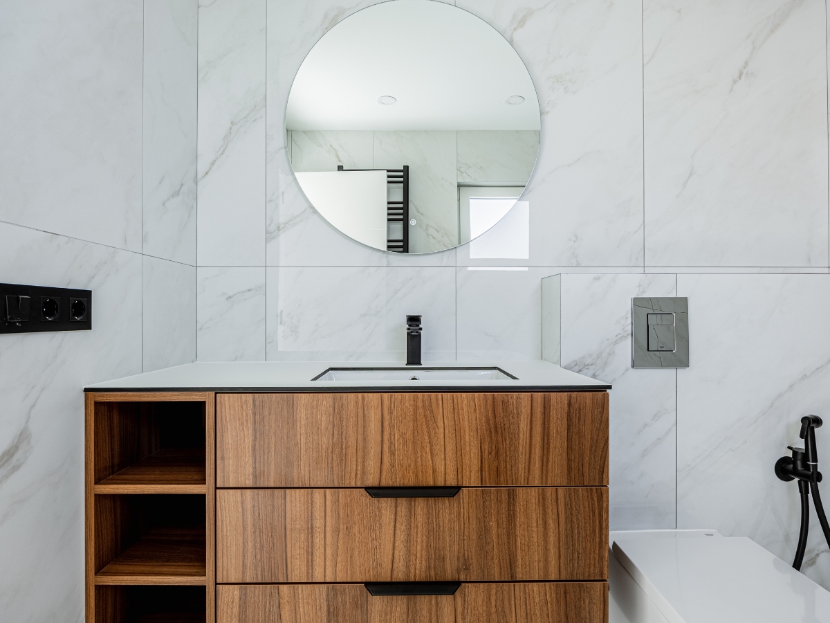 Transform Your Bathroom with a Modern Bathroom Vanity in Buckhead GA 5 Modern bathroom featuring a round mirror above a modern bathroom vanity with drawers, a white countertop, and marble tile walls. A sleek black faucet and built-in shelving complete the stylish design.