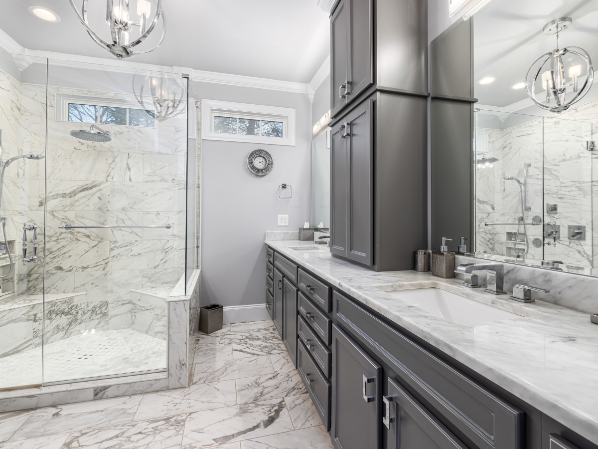 Master Bathroom Remodeling in Vinings: Creating a Luxury Retreat 3 Modern bathroom with gray cabinets, marble countertops and flooring, glass-enclosed shower, dual sinks, and chrome fixtures under bright overhead lighting—perfect for master bathroom remodeling in Vinings.