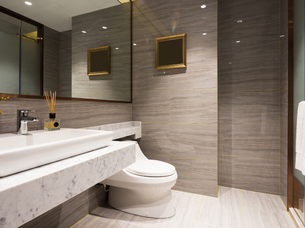 Bathroom Upgrades for the New Year: Best Renovation Ideas in Kennesaw GA 3 Modern bathroom upgrades include a marble sink, white toilet, large wall mirror, two framed pictures, and stylish gray stone tile walls and floor.