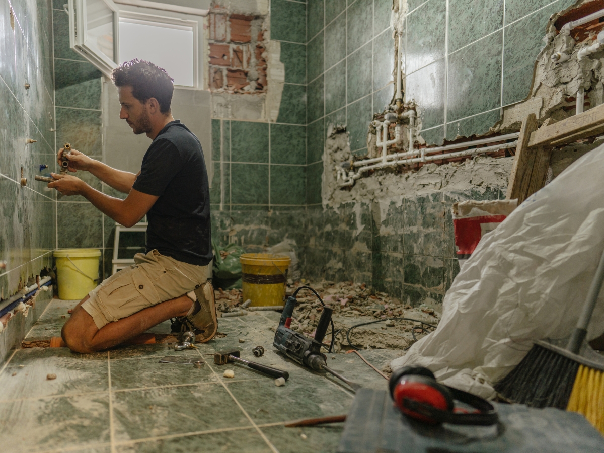Bathroom Upgrades for the New Year: Best Renovation Ideas in Kennesaw GA 5 A man kneels on the floor of a partially renovated bathroom, working on plumbing as tools and construction materials surround him—a hands-on approach to bathroom upgrades.