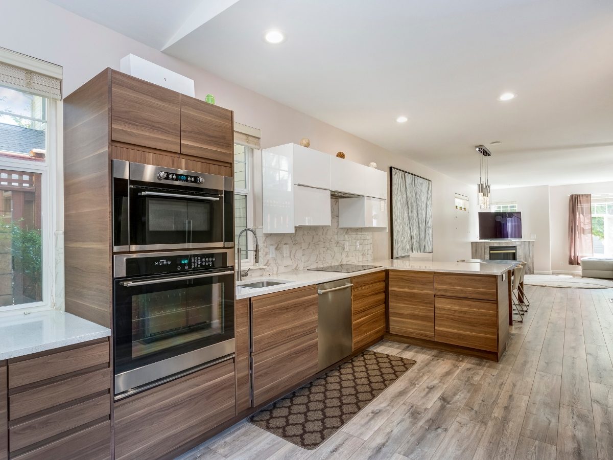 Holiday Home Upgrades: Kitchen Remodeling in Smyrna GA for Festive Gatherings 2 Modern kitchen with wood cabinets, stainless steel appliances, white countertops, tile backsplash, and wood flooring—ideal for holiday home upgrades—connected to an open living area filled with natural light.