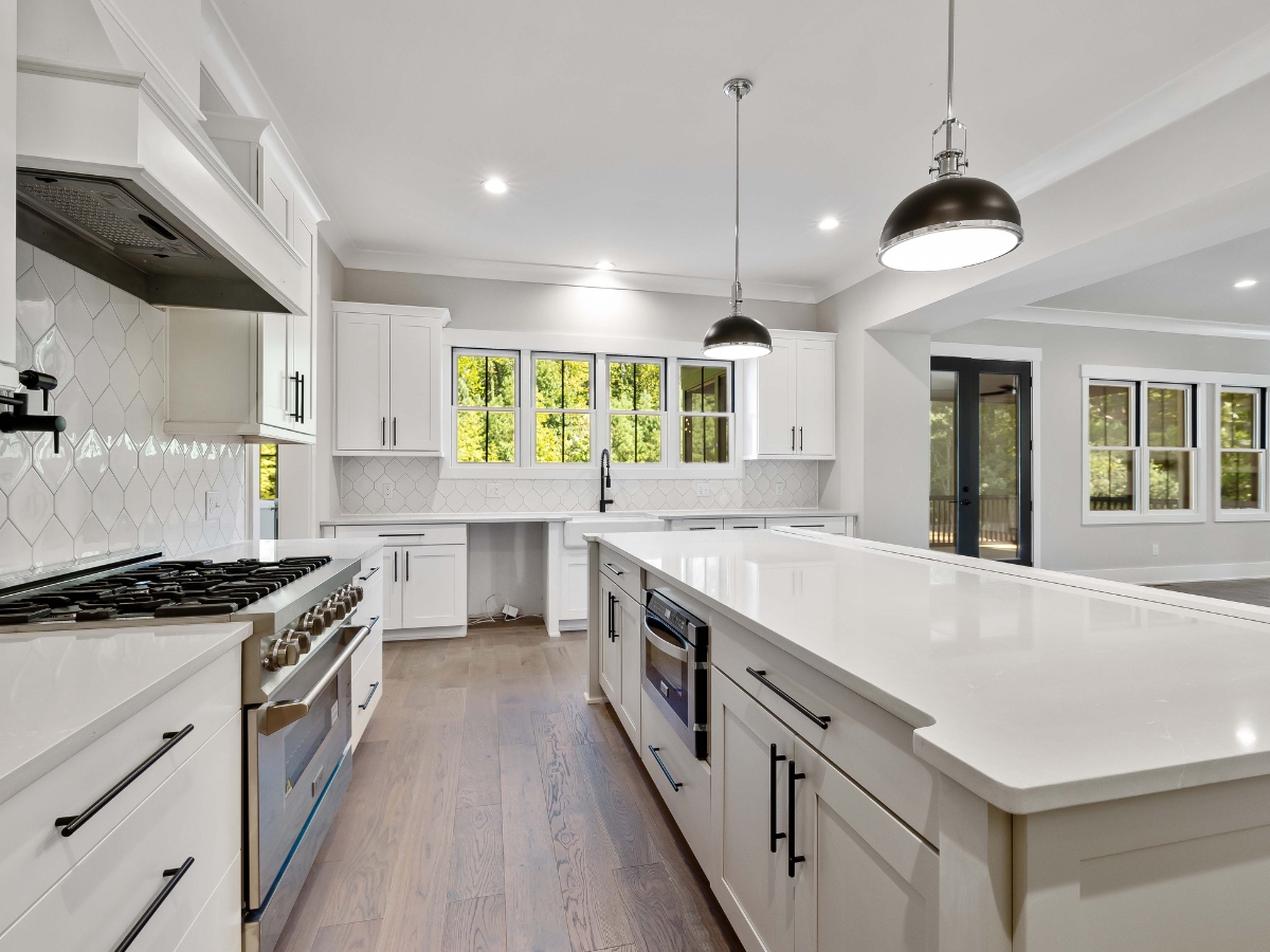 Modern kitchen with white cabinets, stainless steel appliances, large island, pendant lights, and multiple windows letting in natural light—showcasing luxury kitchen design features throughout.