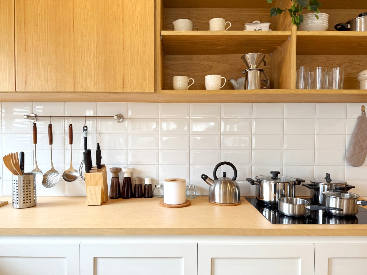 Essential Tips for Organizing Kitchen Cabinets 8 Modern kitchen with wooden shelves, white tiles, various utensils, cookware on the stove, a kettle, and neatly arranged dishes—perfect inspiration if you’re looking for tips for organizing kitchen cabinets.