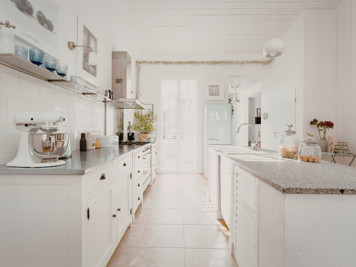 Bright, modern kitchen with white cabinets, a mixer on the counter, light tile flooring, large windows with shutters, and a mint green refrigerator—perfect inspiration for budget kitchen staging ideas.
