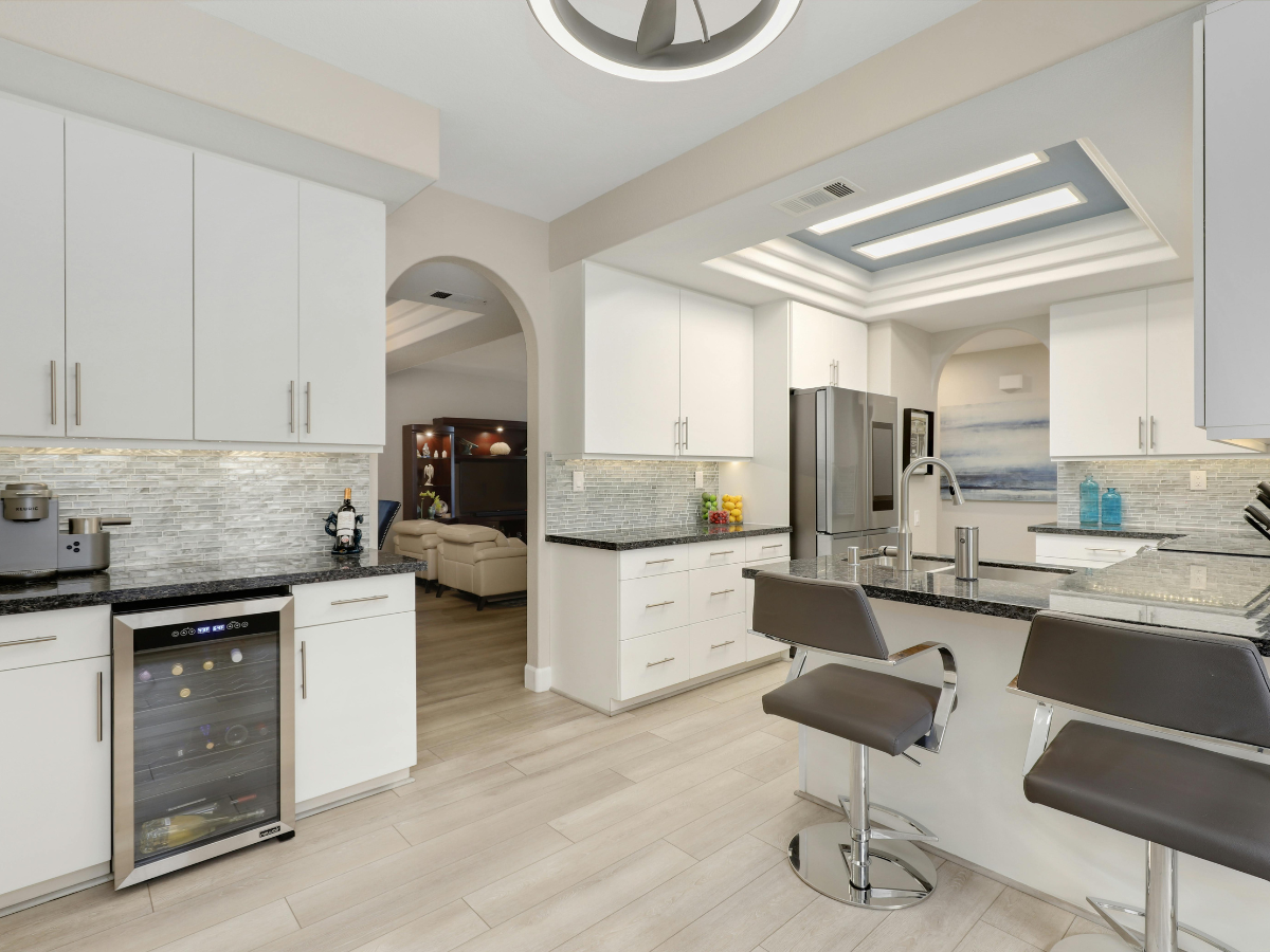 Modern kitchen with white cabinets, stainless steel appliances, black countertops, two bar stools, and a view into a living room through an arched doorway—perfect for showcasing budget kitchen staging ideas.