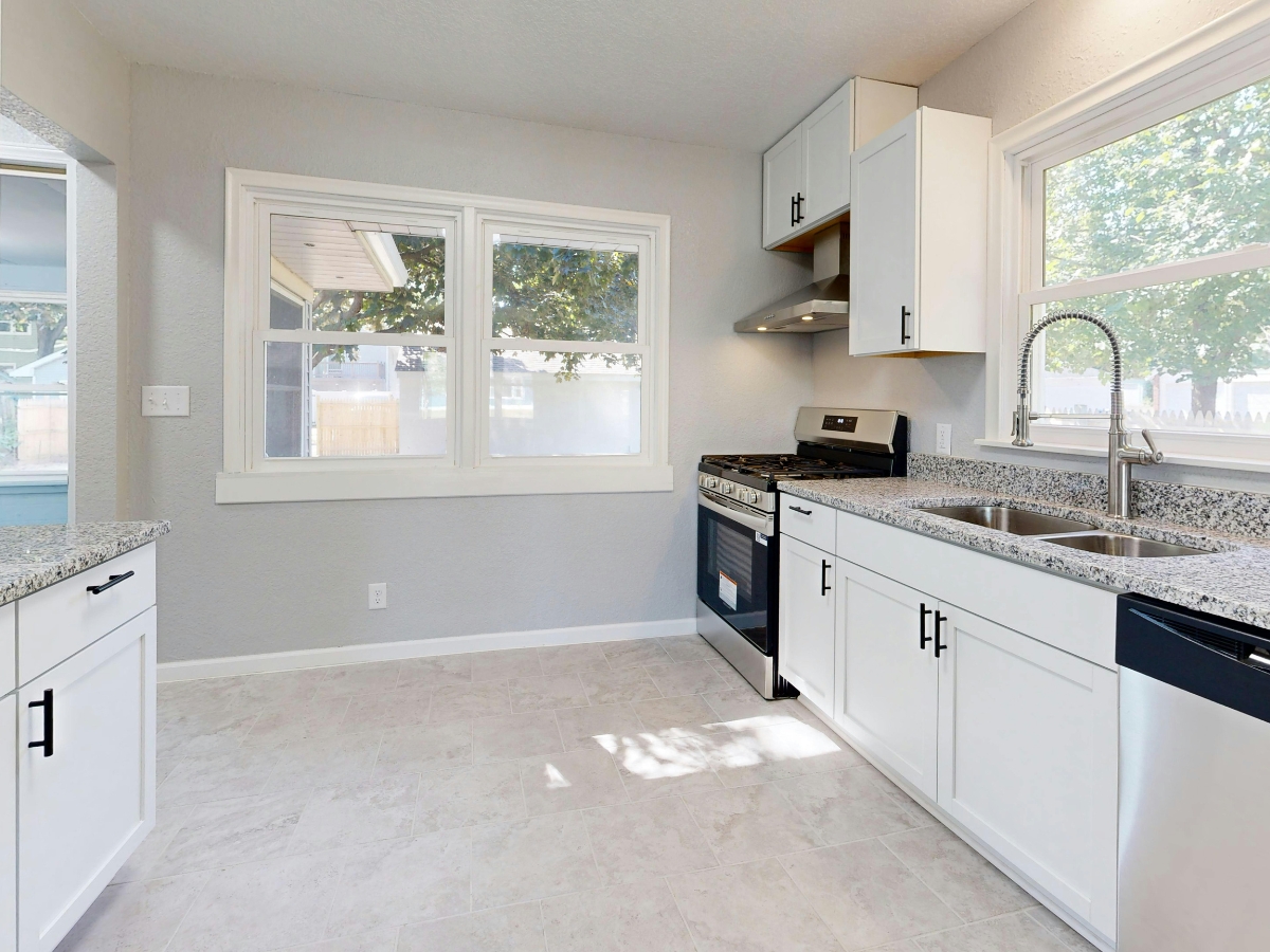 Modern kitchen with white cabinets, granite countertops, stainless steel sink, gas stove, and two windows letting in natural light—free from common Kitchen Staging Mistakes for a truly inviting space.