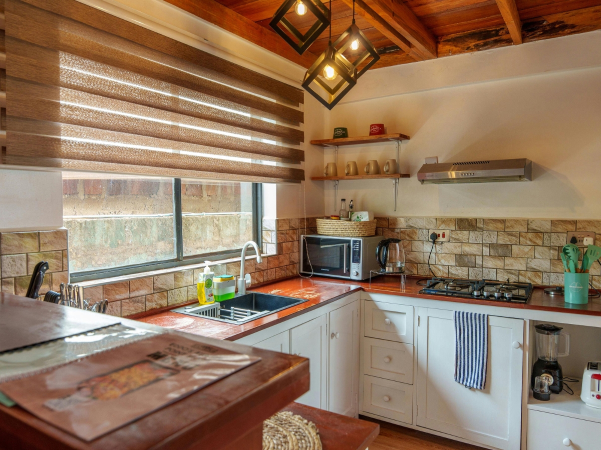 A modern kitchen with white cabinets, a gas stove, a microwave, open shelves with cups, a large window with blinds, and a double sink—free from common kitchen staging mistakes.