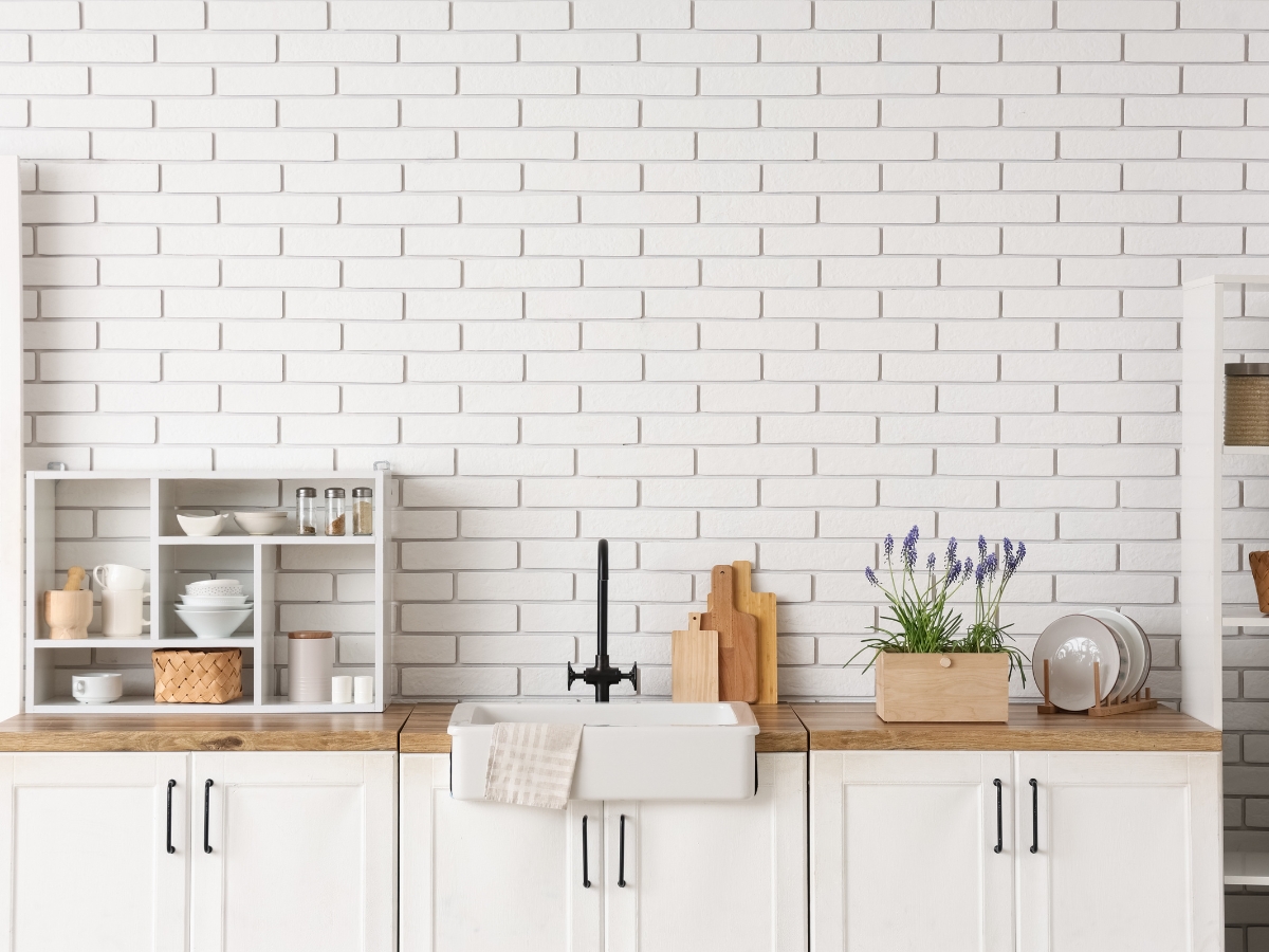 Modern kitchen with white brick wall, wooden countertops, a farmhouse sink, open shelves with dishes, and a potted lavender plant—perfectly avoiding common kitchen staging mistakes.