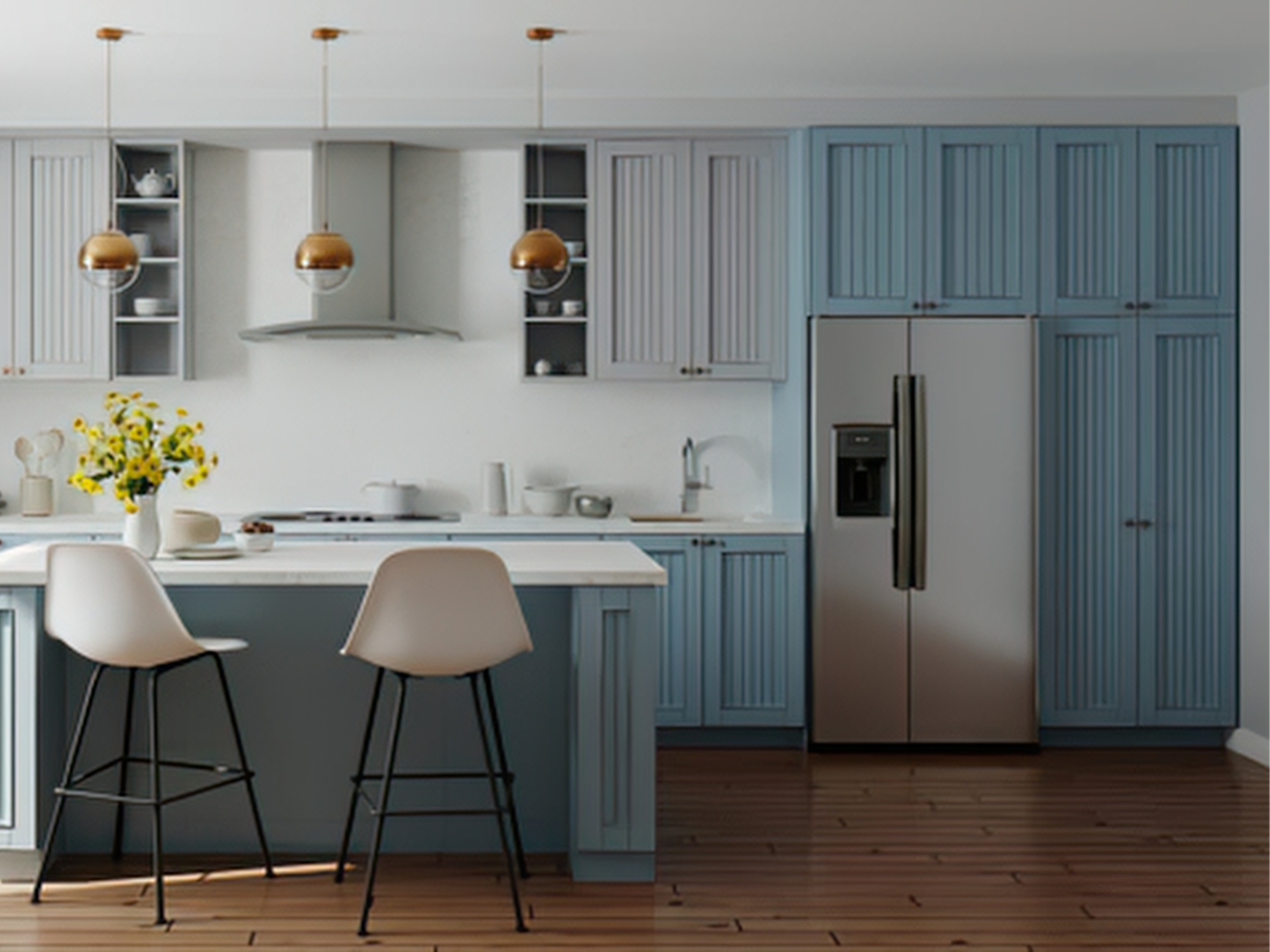 Modern kitchen with blue cabinets—an inspiring example for those looking to choose kitchen colors—features a stainless steel refrigerator, island with two white barstools, pendant lights, and a vase of yellow flowers on the counter.