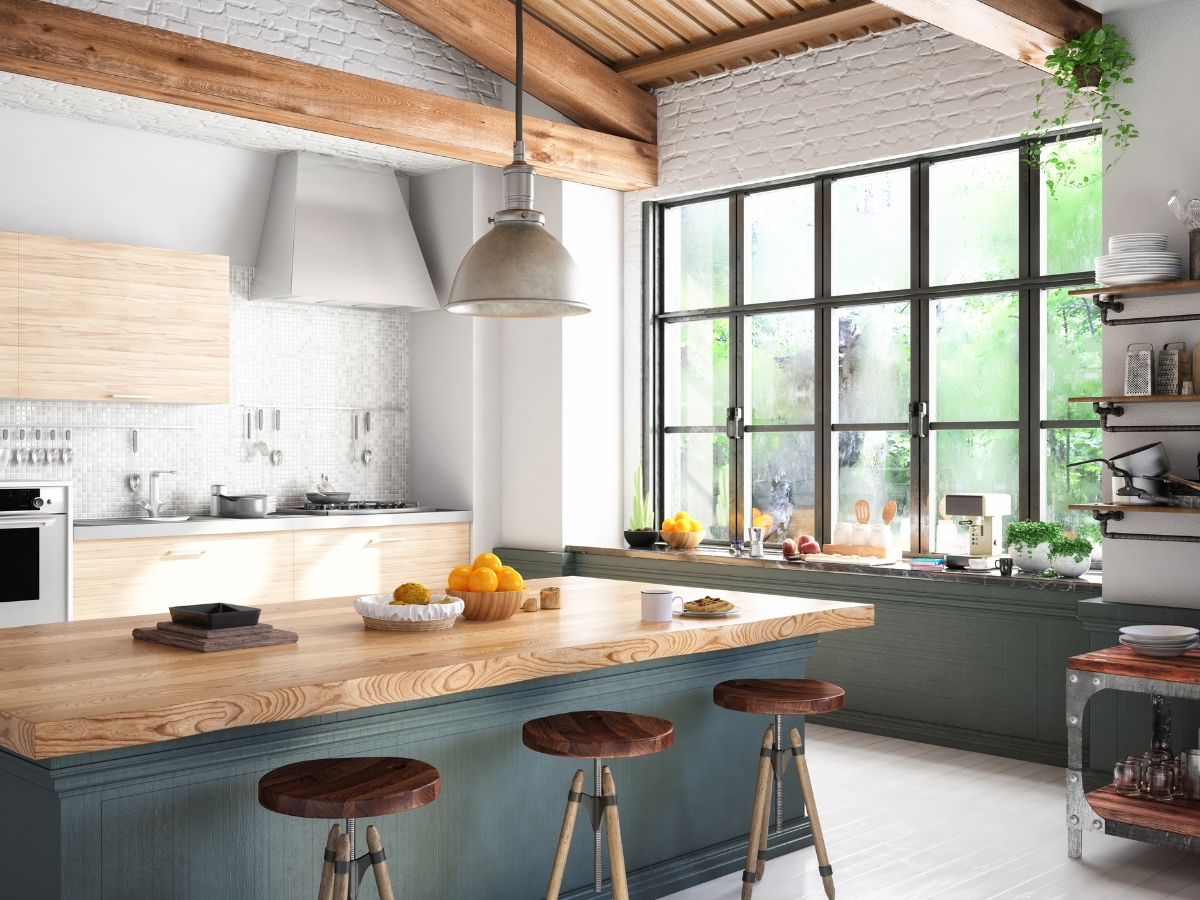 Modern kitchen with wooden beams, large windows, a wooden island with three stools, light wood cabinets, and various dishes and fruits—perfect inspiration to choose kitchen colors that brighten the space and highlight natural textures.